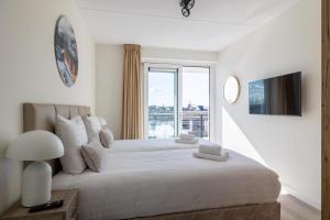 a white bedroom with a large bed with a window at Vakantiewoning aan het strand 'Charlotte's Parel' - met tuin en terras - Vista Maris - Nr 44 in Sint Annaland