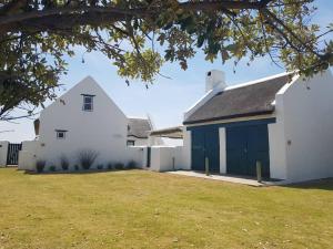 a white house with blue doors and a yard at Ocean Breeze Cottage, Cape Agulhas in Struisbaai