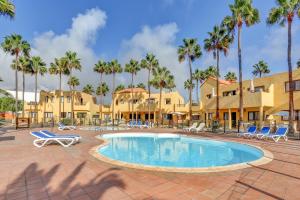 a resort pool with chairs and palm trees at Oasis Royal in Corralejo