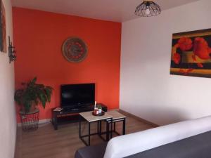 Una sala de estar con una pared naranja con un televisor y una mesa. en Le Camus, en Belonchamp