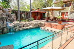 a swimming pool in a yard with a patio and an umbrella at Tudor Lodge Guest House in Johannesburg