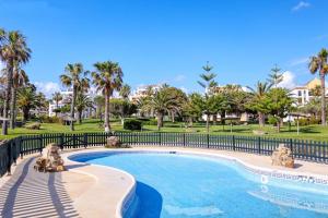 a swimming pool with a fence and palm trees at Apartamento Atlanterra Playa in Zahara de los Atunes