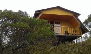 a yellow house on top of a hill with trees at Cabaña Los Llanitos Hospedaje Campestre in Guatavita