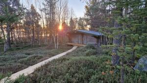 a small cabin in the woods with the sun setting at Hillavilla in the shore of lake Inari in Inari