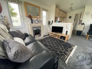 a living room with a black leather couch and a television at Coastal Caravan Holidays - Nightingale 8 in Tunstall