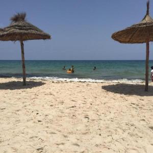 dwa słomiane parasole na plaży z ludźmi w wodzie w obiekcie COSI STUDIO VUE Piscine au bord de la mer à Chott Meriem et dans un emplacement privilégié w mieście Port El Kantaoui