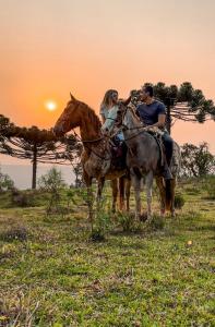 two people riding horses in a field at sunset at Cabana Lago Campestre in Urubici