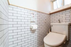 a white tiled bathroom with a toilet and a window at 天下茶屋vii 忙しい旅行中も ゆったりした時間を過ごせるお部屋 お勧めコーヒーと共に in Osaka +30 photos