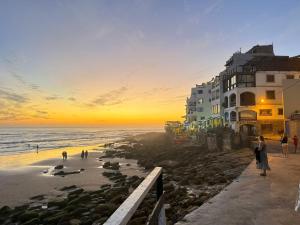 a view of a beach at sunset with a building at Maison de paon - surfstay - relaxstay in Tamraght Ouzdar