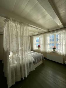 a bedroom with a bed with white curtains and two windows at Nyrestaurert hus fra 1700-tallet in Bjørgo
