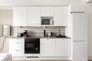 a white kitchen with white cabinets and a microwave at Kotimaailma Apartments Pukkila - New studio for 2 in Turku