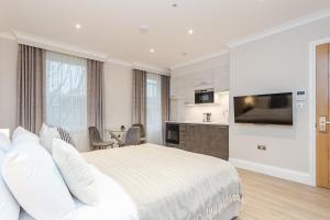 a white bedroom with a bed and a kitchen at Cleveland Residences Chelsea in London