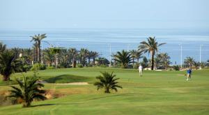 two people playing golf on a green with the ocean in the background at ÁticoToyoAlmeria in Retamar