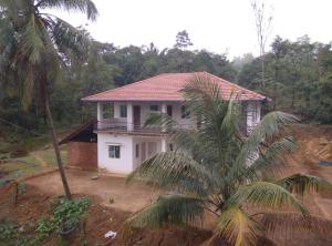 a white house with a palm tree in front of it at Gubbikanta Homestay in Aralagodu