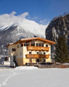 a building in the snow with mountains in the background at Apart Luca in Längenfeld