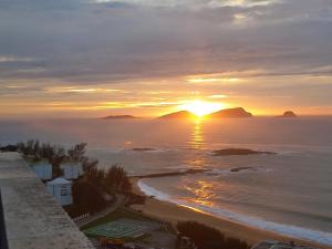 a sunset over the ocean with mountains in the distance at Flats Via Mar in Macaé