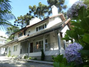 uma casa branca com varanda e flores roxas em Residencial Jardim dos Pinheiros 279 em Canela