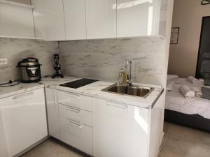 cocina con armarios blancos, fregadero y cama en Apartament Tirana Contact, en Tirana