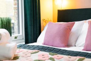 a bed with pink and white pillows and a window at 1BR Stylish Flat by HostaraHomes, Near Liverpool Street, Prime London Location, Sleeps up to 4 in London