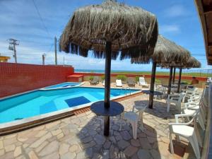 a resort with a swimming pool and an umbrella and chairs at Flat beira-mar em Búzios-RN in Armação dos Búzios