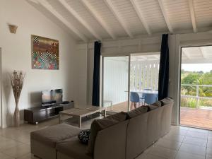 a living room with a couch and a table and a television at Villa Jardin- Les Villas Bleues in Dubédou
