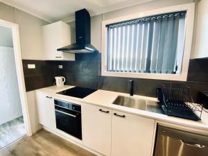 a kitchen with white cabinets and a sink and a window at The Sea Urchin in Tuross Heads +4 photos