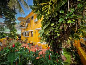 a yellow house with a tree and some plants at Minria Guest House in Benaulim