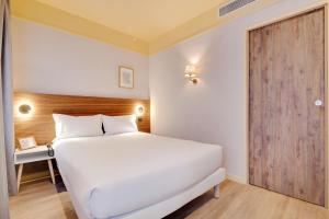 a bedroom with a white bed and a wooden door at Hôtel Cocoon in Saint-Ouen
