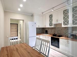a kitchen with white cabinets and a wooden table at Premium Residence, steps to center Arbat, drinking water as a gift in Almaty