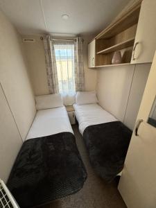 zwei Betten in einem kleinen Zimmer mit Fenster in der Unterkunft Palm Grove 121 - Golden Palm Resort - Pet friendly, WiFi, close to beach and clubhouse - Meadow Lakes Caravan & Lodge Hire in Chapel Saint Leonards
