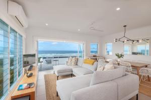 a living room with a white couch and a dining room with the ocean at 4-18 Peregian Esplanade, Peregian Beach QLD 4573 in Peregian Beach