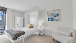 a white bedroom with a bed and a chair at Waterfront On Market in Merimbula