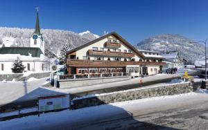 a large wooden building with a church in the snow at Hotel Sonne in Wildhaus
