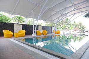 ein Schwimmbecken mit gelben Stühlen und einem weißen Sonnenschirm in der Unterkunft Point C Hotel in Bandung