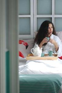 a woman sitting in a bed holding a tray with a cup at El Patio del Limonero in Écija