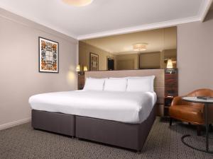 a hotel room with a large bed and a chair at Strand Palace in London