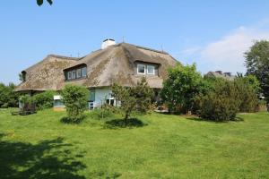 una casa con techo de paja y techo de hierba en un campo en Teewelkenhüs Wiesenappartement, en Archsum