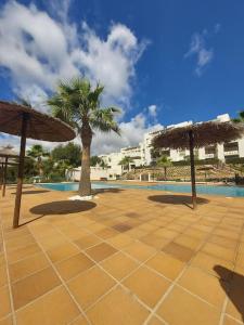 a pool with two umbrellas and a palm tree at Las Colinas Golf Club Residences Casa Encina 1 in Orihuela Costa