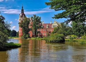 a large red building with a clock tower next to a river at Blütenhaus im Rhododendronpark 5 min zum See in Kromlau