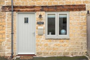un edificio de ladrillo con una puerta blanca y una ventana en Little Gem Cottage Luxury cottage Bourton, dog friendly, parking, Gdn, en Bourton on the Water