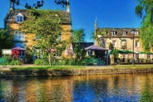 a large building next to a body of water at Hideaway Cottage, Luxury, parking, study, EV in Bourton on the Water