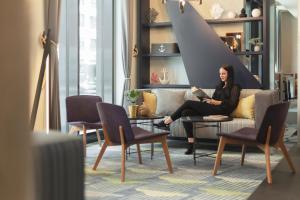 a woman sitting on a couch in a living room at Holiday Inn - the niu, Yen Hamburg City by IHG in Hamburg