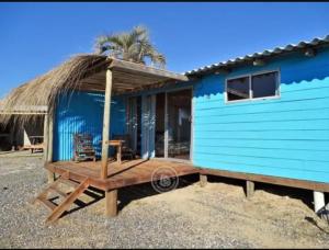 a blue house with a table and a thatched roof at Vida buena in Punta Del Diablo