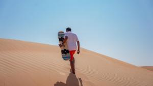 a man holding a skateboard in the desert at Infinity Camp in Bidiyah