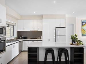 een keuken met witte kasten en een groot eiland met krukken bij Oceans 10 in Ocean Grove