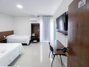 a hotel room with two beds and a desk and a television at Hotel Minas in Três Marias