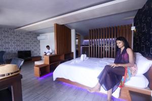 una mujer sentada en una cama en una habitación de hotel en Ripple Beach Inn, en Hulhumale