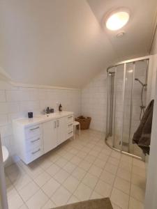 a white bathroom with a shower and a sink at Stort landsted med egen strand in Rød