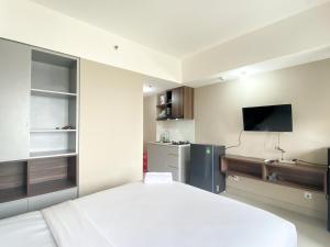 une chambre avec un lit blanc et une télévision dedans dans l'établissement Well Furnished and Cozy Studio at Gateway Park LRT City Jatibening Apartment By Travelio, à Bekasi