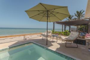 a pool with chairs and an umbrella next to the ocean at Playa Turix Villa in Chicxulub